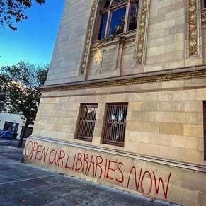 library exterior with graffiti: OPEN OUR LIBRARIES NOW